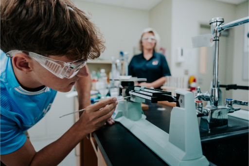 a student wearing safety goggles and looking at a microscope